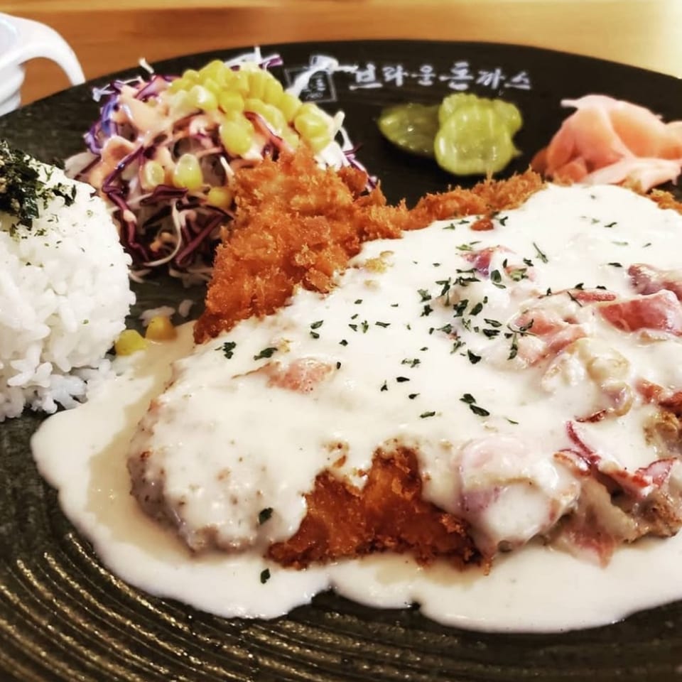 Cafe Mixx's tonkatsu with creamy sauce, rice, salad, and pickled ginger on a dark plate.
