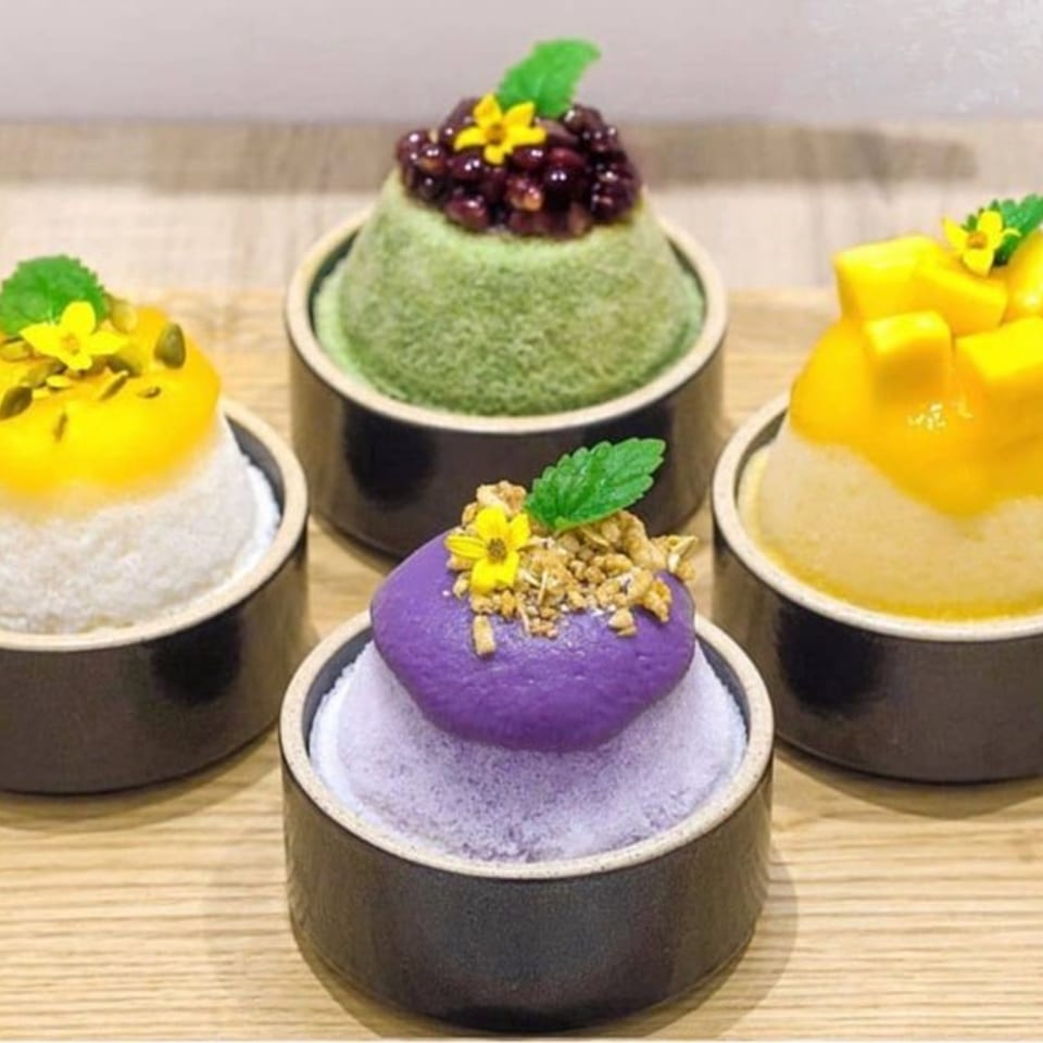 Four colorful Cafe Mixx shaved ice desserts with various fruit and toppings in dark bowls.