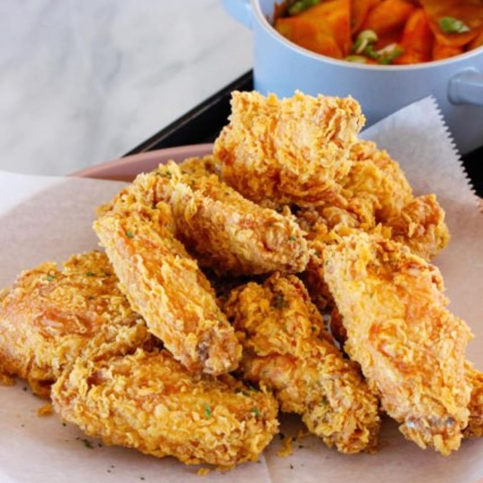 Crispy golden fried chicken wings on parchment paper, with a blue bowl of stew in the background.