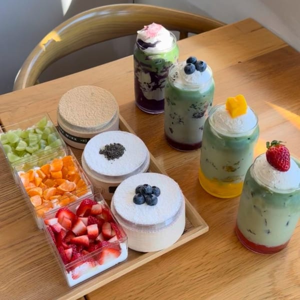 Cafe Mixx desserts and drinks, including matcha lattes, cheesecakes, and fresh fruit on a wooden table.