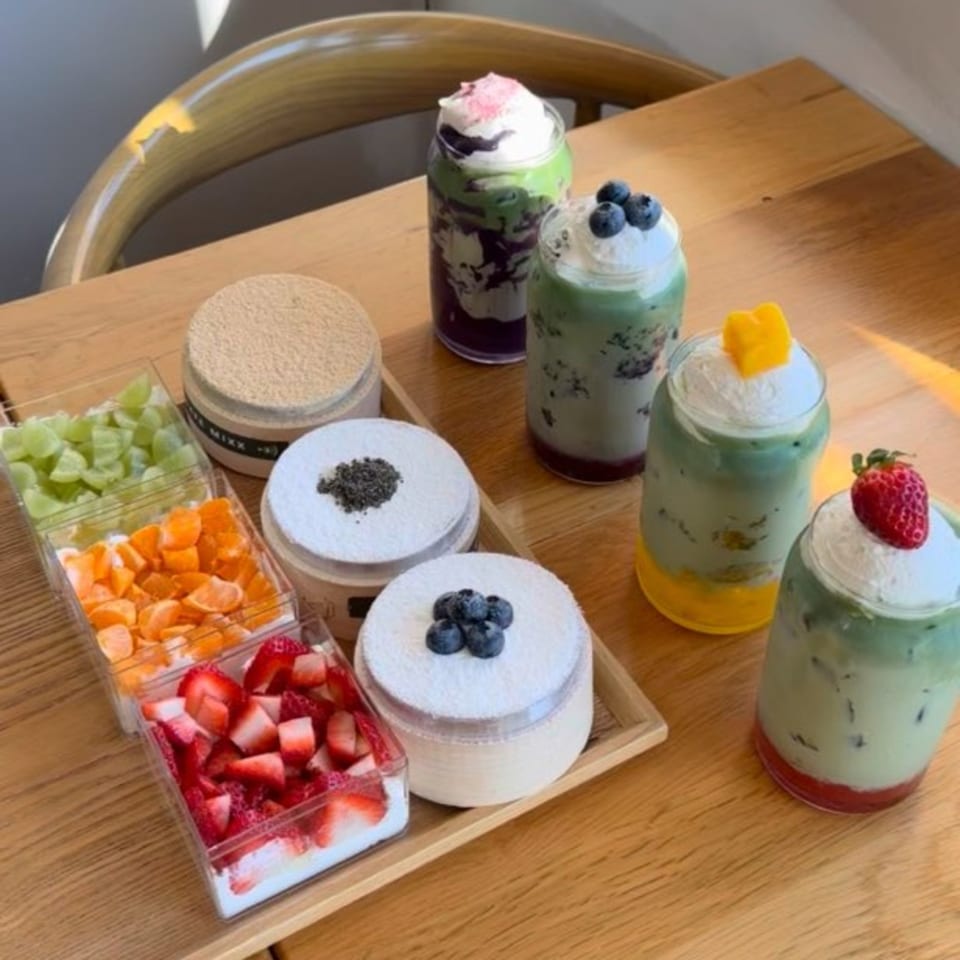 Cafe Mixx desserts and drinks on a wooden table, including fruit cups, cakes, and layered beverages.